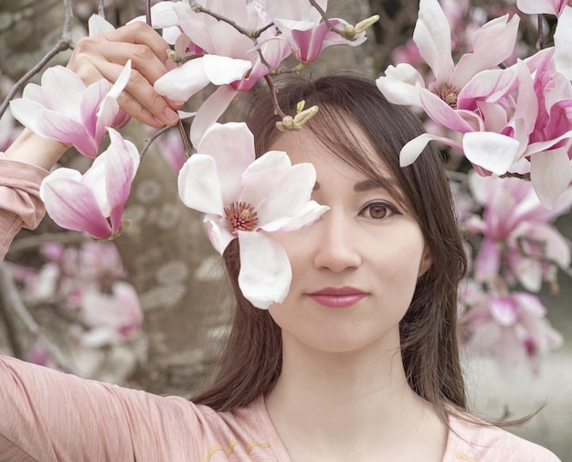 Portrait d'une belle jeune femme dans un jardin japonais avec des fleurs de magnolia rose en fleurs