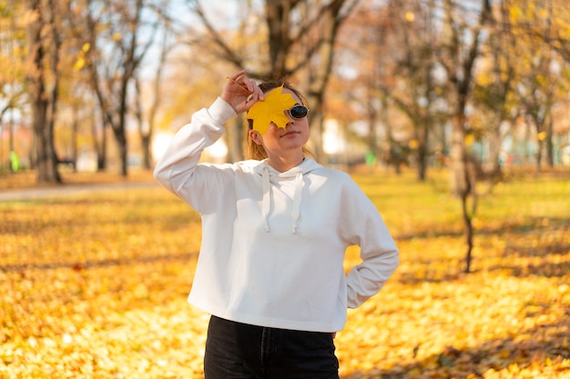 Portrait de la belle jeune femme dans un pull blanc et des lunettes de soleil marchant à l'extérieur à l'automne.