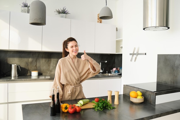 Portrait d'une belle jeune femme dans ses vêtements de maison coupant des légumes tenant un couteau et coupant