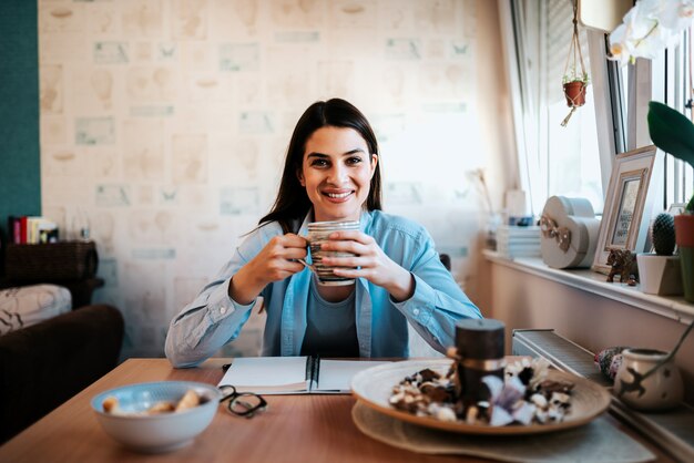 Portrait de la belle jeune femme dans son appartement en buvant du café.