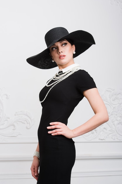 Portrait d'une belle jeune femme dans un style rétro dans un élégant chapeau noir et robe sur mur de luxe rococo