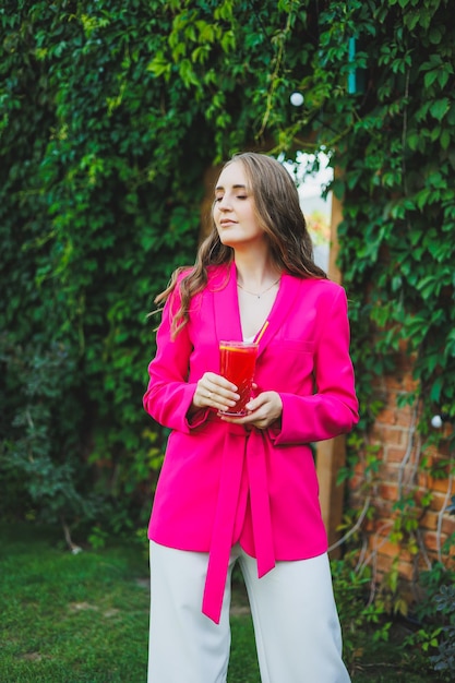 Portrait d'une belle jeune femme dans une veste rose vif avec un cocktail dans les mains Une femme heureuse souriante buvant de la limonade rafraîchissante sur la terrasse d'un café d'été