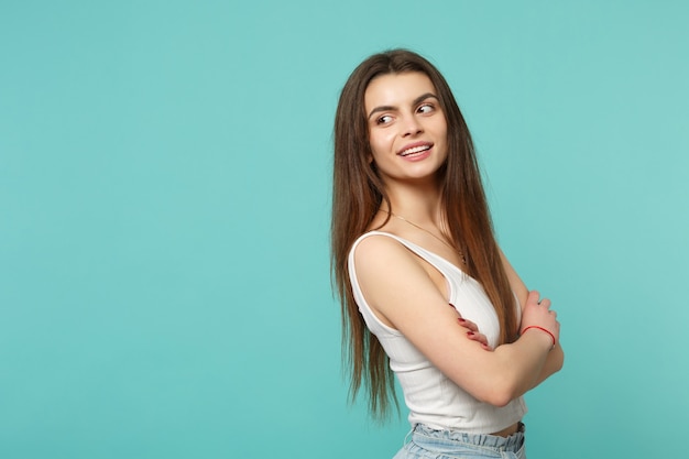 Portrait d'une belle jeune femme dans des vêtements légers et décontractés regardant de côté, tenant les mains croisées isolées sur fond de mur bleu turquoise. Concept de mode de vie des émotions sincères des gens. Maquette de l'espace de copie.