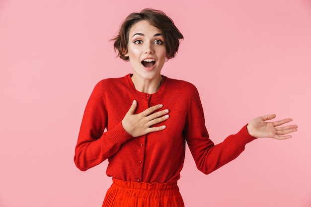 Portrait d'une belle jeune femme excitée portant des vêtements rouges debout isolé sur fond rose