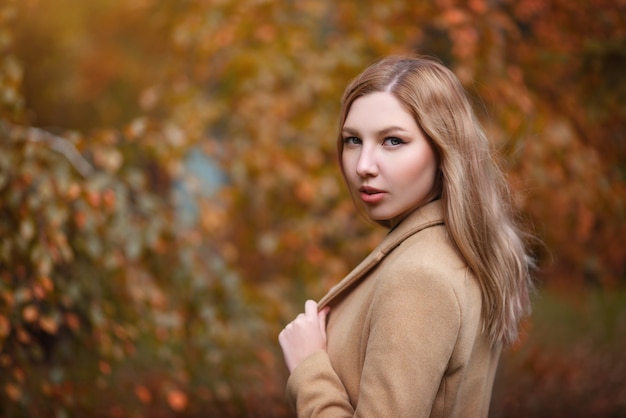 Portrait d'une belle jeune femme fille blonde dans un manteau beige sur le parc en automne