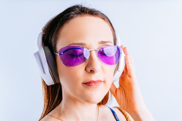 Portrait de belle jeune femme sur fond blanc portant des lunettes d'été, écouter de la musique avec des écouteurs sans fil. concept partir en vacances