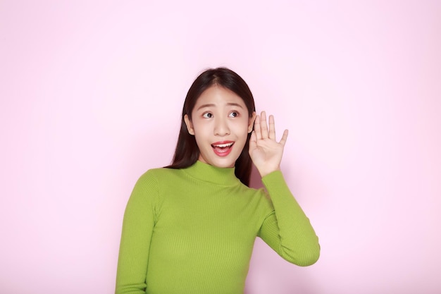 Portrait d'une belle jeune femme sur un fond rose clair heureuse et souriante posant en position debout femme asiatique faisant des gestes en chuchotant