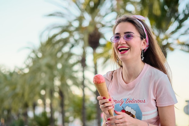 Portrait de la belle jeune femme heureuse en lunettes de soleil roses mangeant une glace rose.