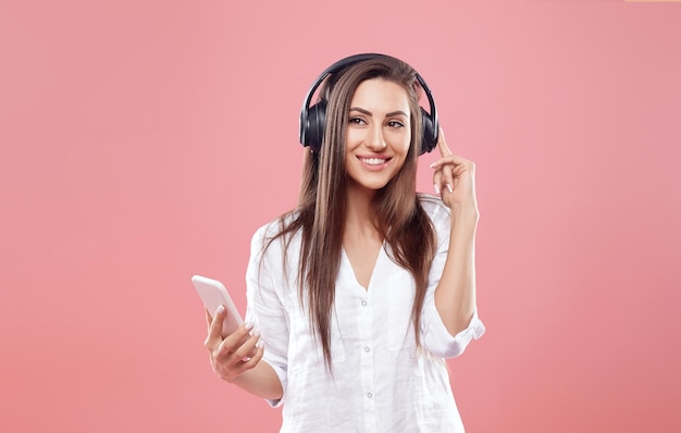 Portrait d'une belle jeune femme heureuse posant isolé sur fond de mur rose écoutant de la musique