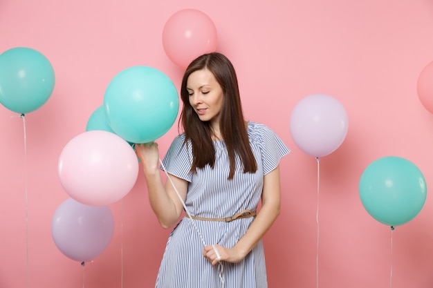 Portrait de la belle jeune femme heureuse tendre en robe bleue tenant des ballons à air colorés regardant vers le bas sur fond rose tendance lumineux. Fête d'anniversaire, concept d'émotions sincères.