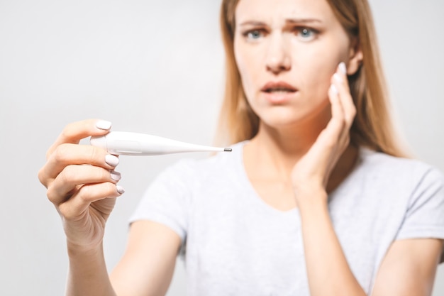 Portrait d'une belle jeune femme inquiète vérifiant sa température. Fond blanc, grippe.