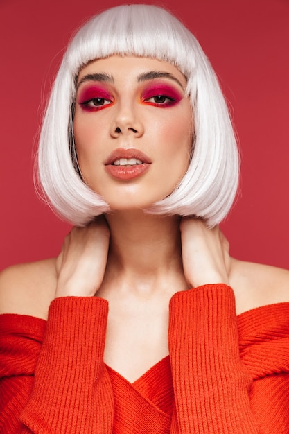 Portrait de belle jeune femme isolée sur mur rouge avec maquillage lumineux posant.