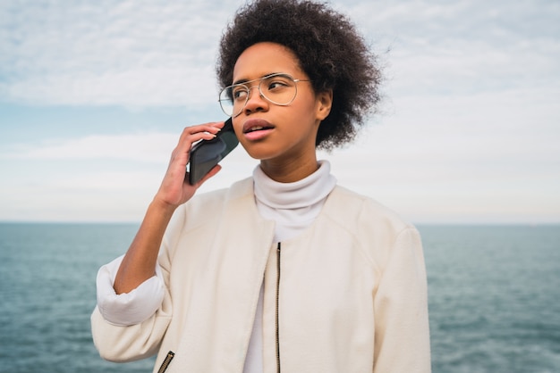 Photo portrait de la belle jeune femme latine parlant au téléphone à l'extérieur avec la mer sur l'espace. concept de communication.