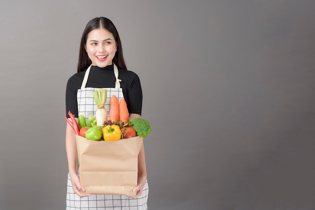 Portrait de la belle jeune femme avec des légumes dans un sac d'épicerie en fond gris studio