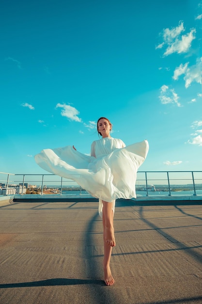 Portrait d'une belle jeune femme en longue robe blanche debout sur le toit d'un immeuble avec paysage urbain