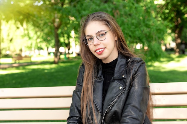 Portrait d'une belle jeune femme à lunettes dans un parc verdoyant d'été assis sur un banc