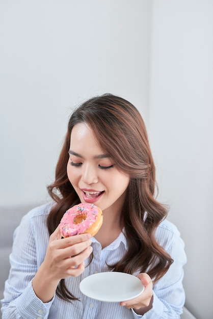 Portrait de belle jeune femme mangeant des beignets à la maison.