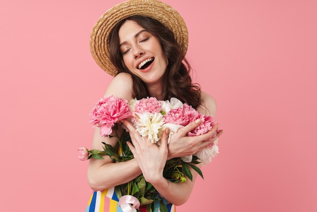 Portrait de la belle jeune femme mignonne souriante heureuse posant isolée sur un mur rose tenant des fleurs