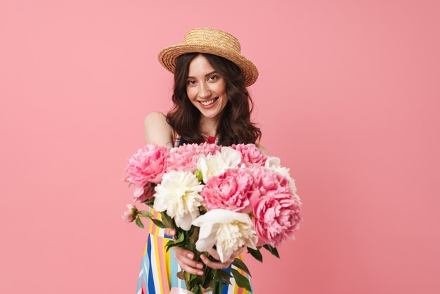 Portrait de la belle jeune femme mignonne souriante positive posant isolée sur un mur rose tenant des fleurs