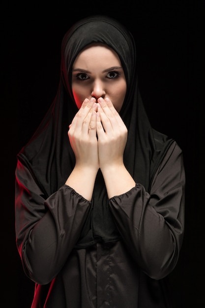 Portrait de belle jeune femme musulmane sérieuse portant un hijab noir avec les mains près de son visage en tant que concept noir