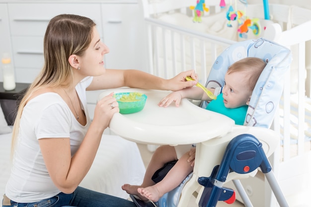 Portrait d'une belle jeune femme nourrissant un bébé de 9 mois assis dans une chaise haute