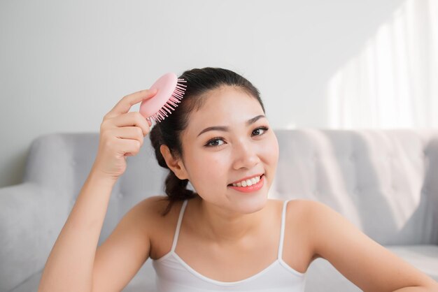 Portrait de belle jeune femme peignant ses cheveux, regardant la caméra et souriant