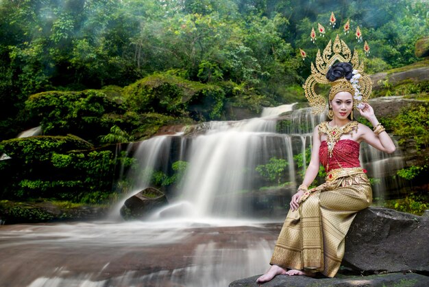 Photo portrait d'une belle jeune femme portant une couronne et des vêtements traditionnels assise contre une chute d'eau dans la forêt