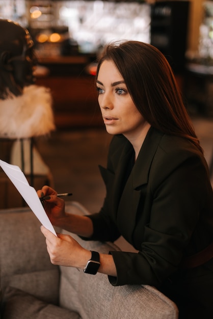 Portrait d'une belle jeune femme portant des vêtements élégants dans un restaurant tenant des documents papier