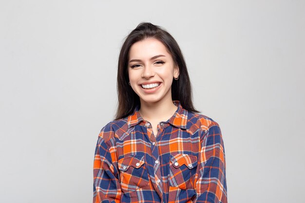 Portrait de belle jeune femme Portrait d'une belle brune souriante dans une chemise à carreaux sur un blanc gris