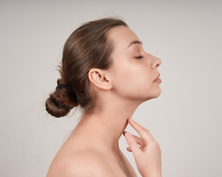 Portrait de belle jeune femme de profil avec les épaules nues, touchant son cou. mur léger.