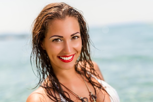 Portrait d'une belle jeune femme profitant de la plage. Elle sourit et regarde la caméra.