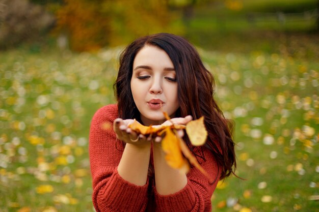 Portrait de belle jeune femme en pull tricot rouge souffle feuilles