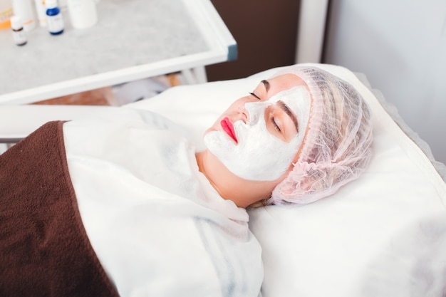 Portrait de la belle jeune femme qui applique un masque facial. Procédure cosmétique dans le salon de spa. Soins de la peau du visage.