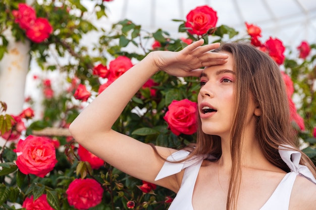 Portrait de la belle jeune femme regardant avec la main sur son front sur les fleurs