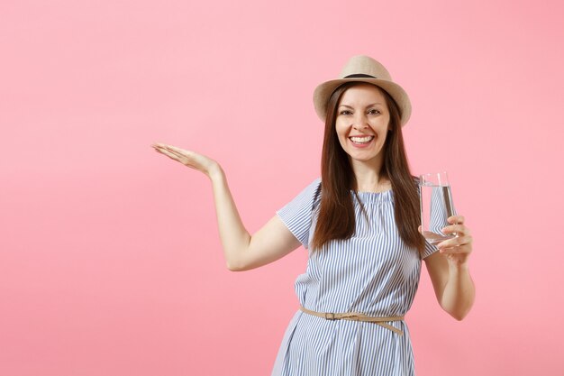 Portrait D'une Belle Jeune Femme En Robe Bleue, Chapeau Tenant Et Buvant De L'eau Pure Fraîche Et Claire En Verre Isolé Sur Fond Rose. Mode De Vie Sain, Personnes, Concept D'émotions Sincères. Espace De Copie