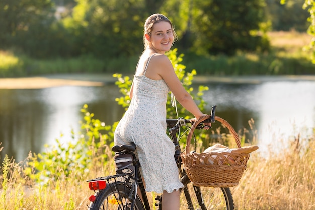 Portrait de belle jeune femme en robe courte à vélo au bord du lac au coucher du soleil