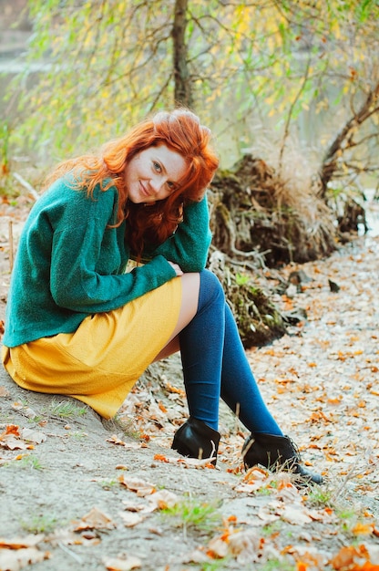 Portrait d'une belle jeune femme rousse aux taches de rousseur, yeux bleus dans le parc d'automne. Pull vert.