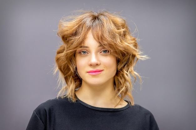 Portrait d'une belle jeune femme rousse caucasienne avec une courte coiffure ondulée souriant et regardant la caméra sur fond gris foncé avec espace de copie