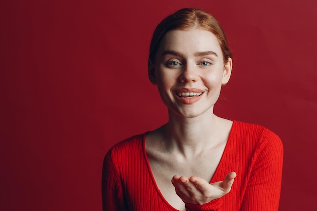 Portrait d'une belle jeune femme rousse soufflant des baisers sur fond rouge