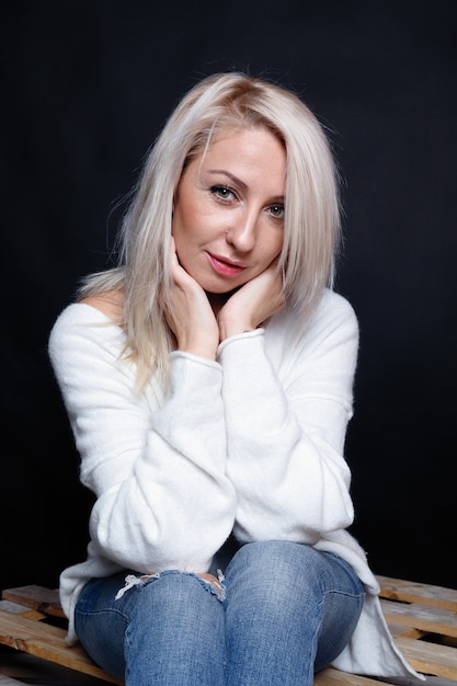 Portrait d'une belle jeune femme séduisante dans un pull blanc aux yeux bleus et aux longs cheveux blonds.