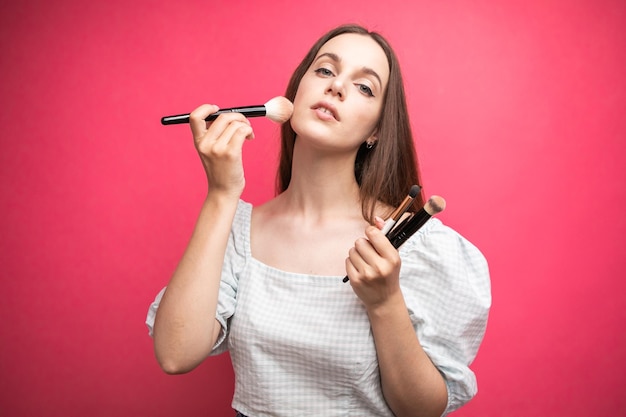 portrait d'une belle jeune femme séduisante debout isolée sur fond rose, tenant le maquillage