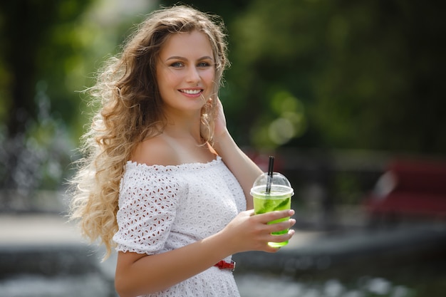 Portrait d'une belle jeune femme séduisante à l'extérieur en été avec un verre de jus glacé ou une boisson. Jolie fille dehors avec mojito frais