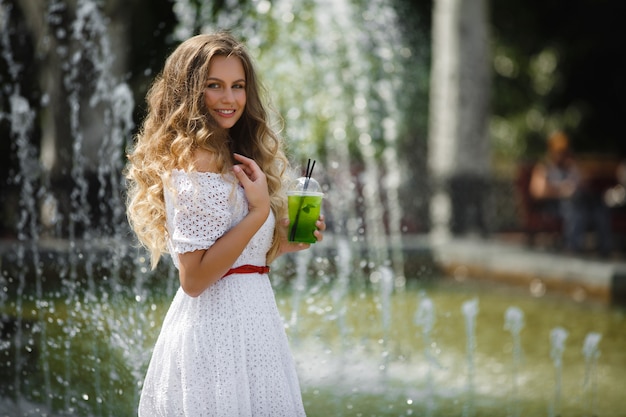 Portrait d'une belle jeune femme séduisante à l'extérieur en été avec un verre de jus glacé ou une boisson. Jolie fille dehors avec mojito frais