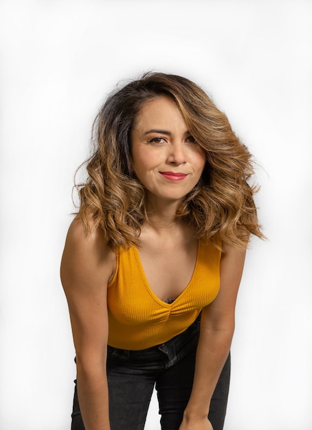 Portrait d'une belle jeune femme souriante et confiante debout avec désinvolture vêtue d'un chemisier jaune et d'un jean noir isolé sur fond blanc