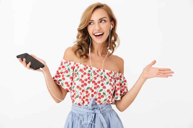 Portrait d'une belle jeune femme souriante en écoutant de la musique avec des écouteurs et un smartphone isolé