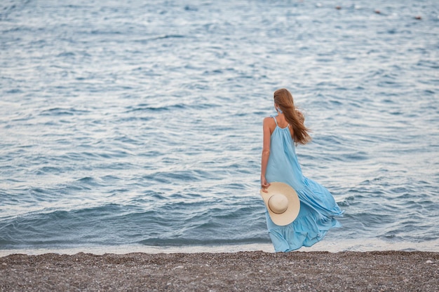 Portrait d'une belle jeune femme souriante portant un chapeau de paille sur la plage avec la mer en arrière-plan Fille de mode beauté regardant la caméra au bord de la mer Femme bronzée insouciante marchant sur le sable et riant