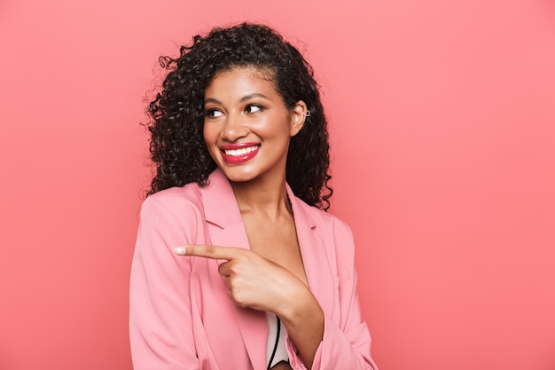 Portrait d'une belle jeune femme souriante portant des vêtements d'été debout isolé sur un mur rose, pointant vers l'espace de copie