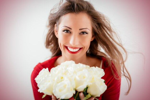 Portrait d'une belle jeune femme souriante tenant un bouquet de roses blanches et regardant la caméra.