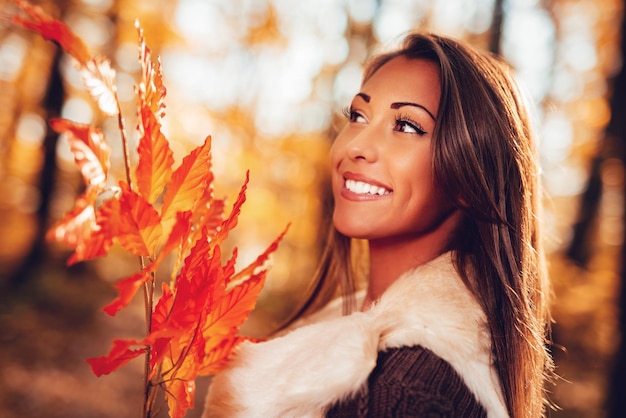 Portrait d'une belle jeune femme souriante tenant des feuilles dans la nature en automne.