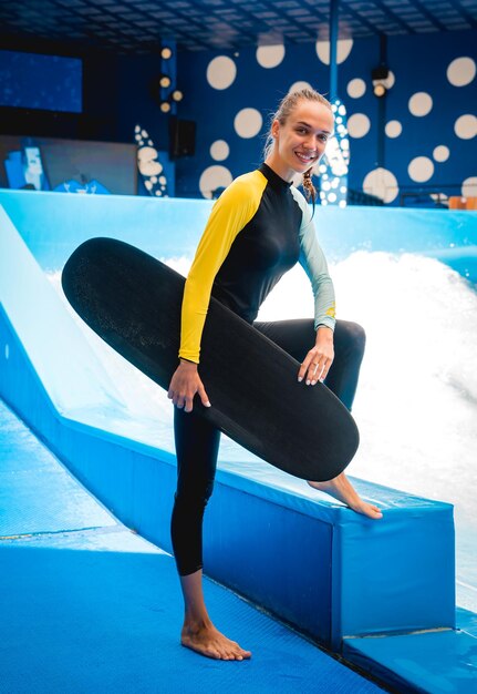 Portrait d'une belle jeune femme avec le surf sur un fond de simulateur de vagues